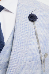 Homme portant un costume gris clair, une cravate bleu marine et une broche à fleur sur fond blanc