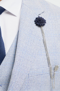 Homme portant un costume gris clair, une cravate bleu marine et une broche à fleur sur fond blanc