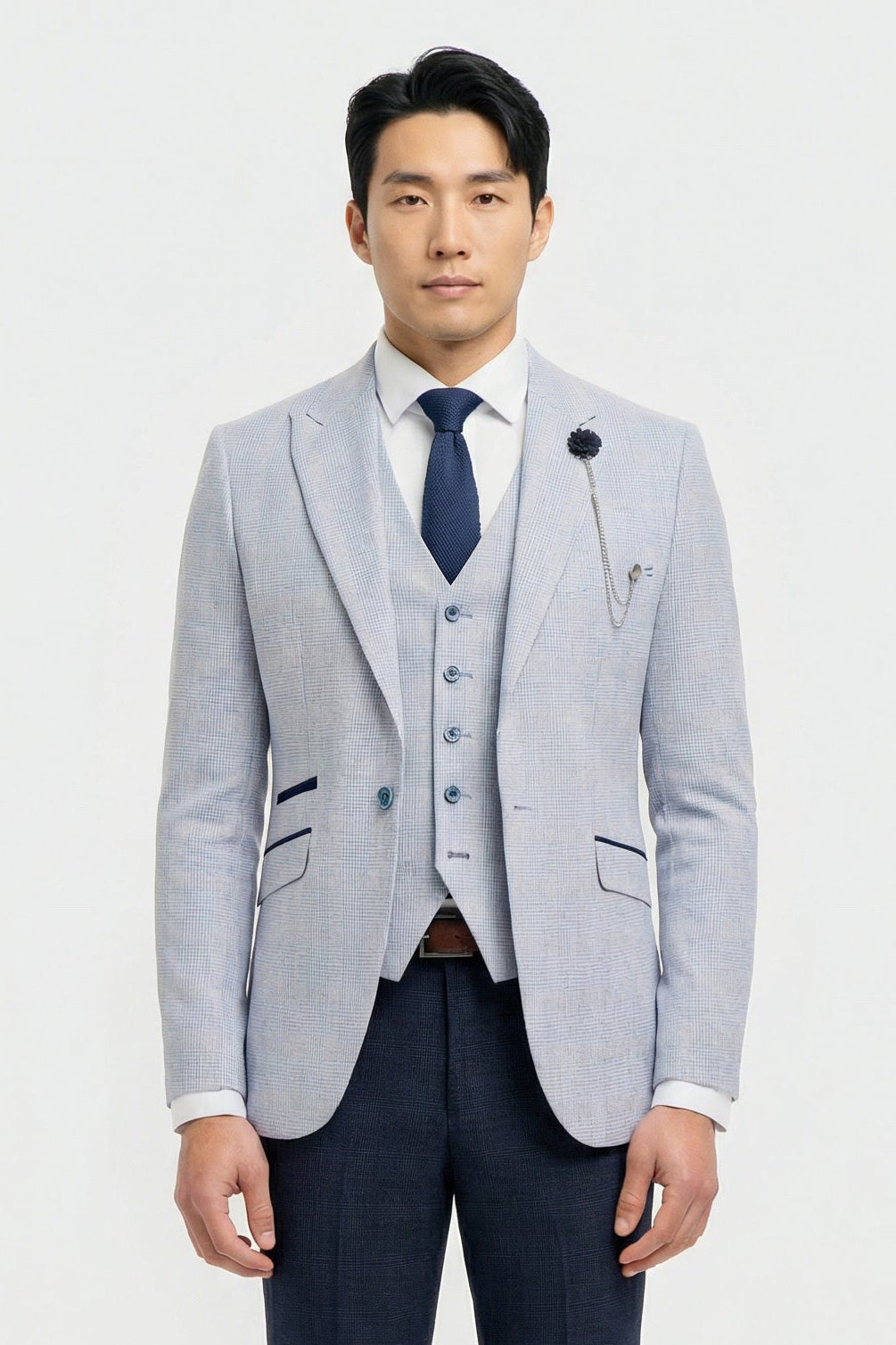Homme portant un blazer gris clair, un gilet bleu marine et une cravate bleu foncé sur fond blanc