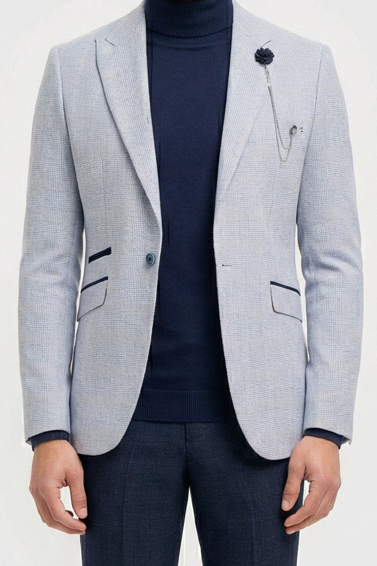 Homme portant un blazer gris clair, un col roulé bleu marine et un pantalon foncé sur fond blanc